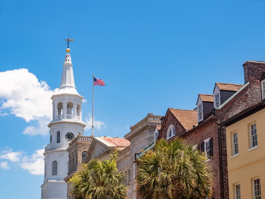 Downtown North Charleston, SC skyline featuring historic architecture, palm trees, and a church steeple beneath a bright blue sky.